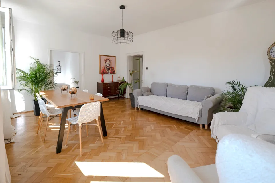 Jadalnia z drewnianym stołem i salon z szarą sofą w domu przy Racławickiej 54 we Wrocławiu