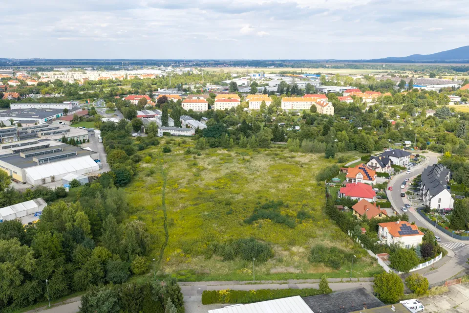 Widok z góry na działkę w Świdnicy otoczoną zielenią, z blokami mieszkalnymi i halami po lewej stronie kadru