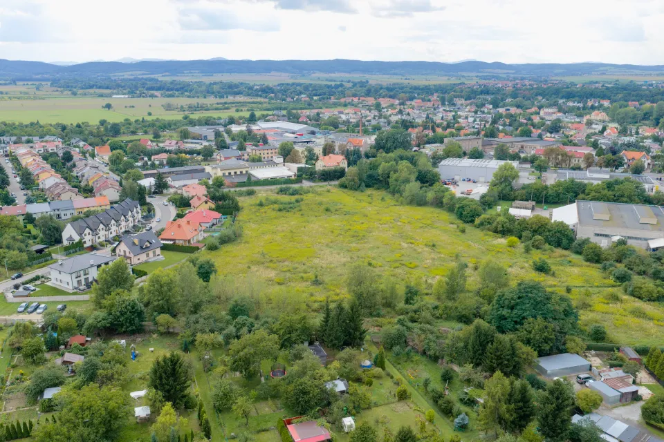 Ujęcie lotnicze działki w Świdnicy od strony ogrodów działkowych, z zabudową miejską i wzgórzami w tle